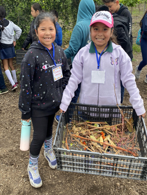 Kinoshita students pose, holding a bin of crops from The Ecology Center's Regenerative Organic CertifiedTM farm.