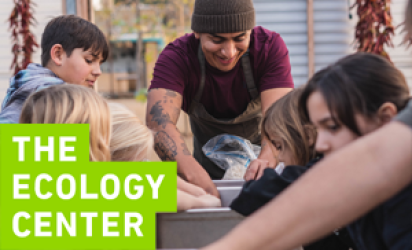Kids experiencing the Ecology Center fermentation lab, with an adult in a toboggan leading the instruction.  All hands are in compost bins. The Ecology Center Logo is on the bottom left of the image. 