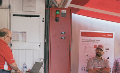 An instructor presenting in front of a group, electronics and refrigeration equipment showing in the foreground and background.