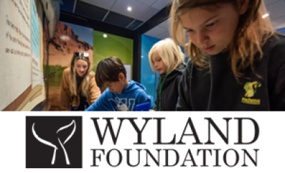 Children examining an exhibit in the Environmental Education center as an instructor looks on. Blues and greens cover the walls, along with imagery of desert landscapes. The bottom third of the image displays the Wyland Foundation logo in black over a white rectangle. 