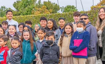 An elementary school class posing for the camera with a backdrop of green shrubs and a purple Trust for Public Land Banner off to the right of the image.